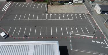 広い駐車場が設けられた右上に更地になった建設予定地を上空から撮影した写真