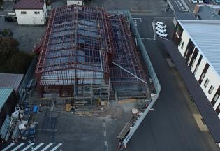 2階部分まで足場が組まれた建設予定地を駐車場側の上空から撮影した写真