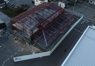 2階部分まで足場が組まれた建設予定地を敷地内に建つ建物側の上空から撮影した写真