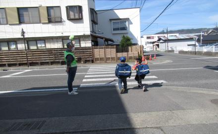 横断歩道を渡る二人の子供を見守る男性の写真