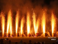 法被を着た人達が横2列に並び、手筒花火からオレンジ色の火柱が上がっている写真