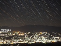 きれいに光る街の夜景と、たくさんの星がラインを描いている光跡の写真