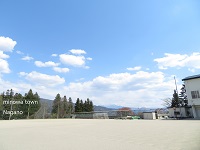 澄んだ青空と、奥に小さくサッカーゴールや倉庫などが映るグラウンドの写真