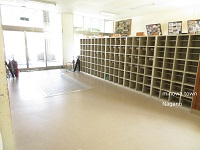正面から光が差し込んでいる玄関と、最上段にイベントの写真が貼られたボードが置いてある下駄箱が並んでいる写真