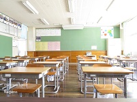 右手の窓から陽の光が差し込む中、教室に並べられている机や椅子を教壇側から撮った写真