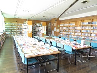 学校の図書館で陽の光が差し込む中、奥に棚があり、手前には本が並んだ机の写真