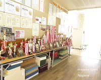 部活動の成果であるたくさんのトロフィーが机の上に、賞状や写真などが壁に飾られている写真