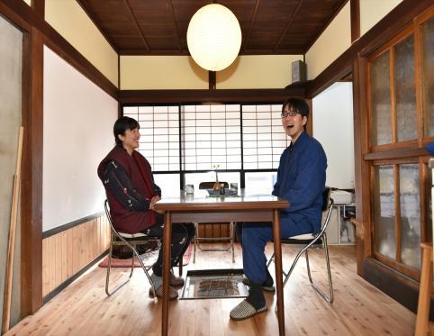 障子の引き戸があり、丸い球状の照明がついている部屋で向かい合って座っている関野さんと奥様の写真